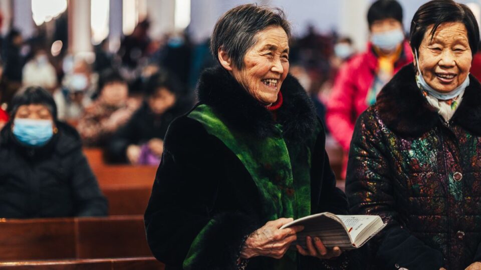 Zwei chinesische Damen. Eine hält eine Bibel in der Hand und lächelt.